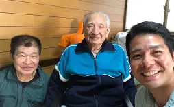 屋外で3人の男性が笑顔で並び、住宅の前で記念撮影している様子