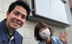 3人の男女が屋外で笑顔を見せ、1人の女性がカーネーションを手にしている
